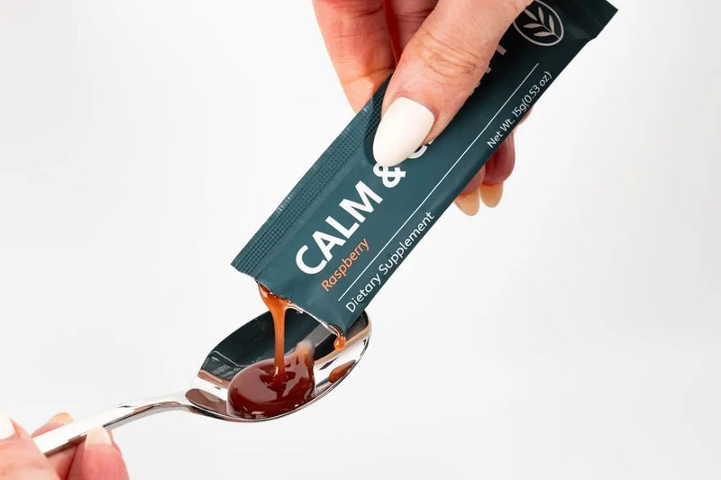 Hand holding a 'Calm &' dietary supplement packet with a spoonful of liquid.