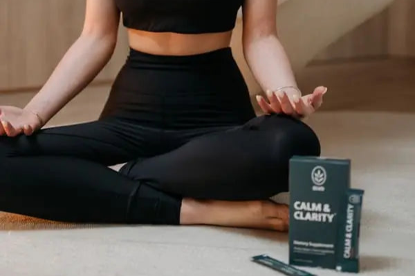 Women in black athletic wear sitting on the floor with 'Calm & Clarity' supplement box.